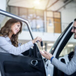 Car dealer and customer at vehicle showroom choosing new car.